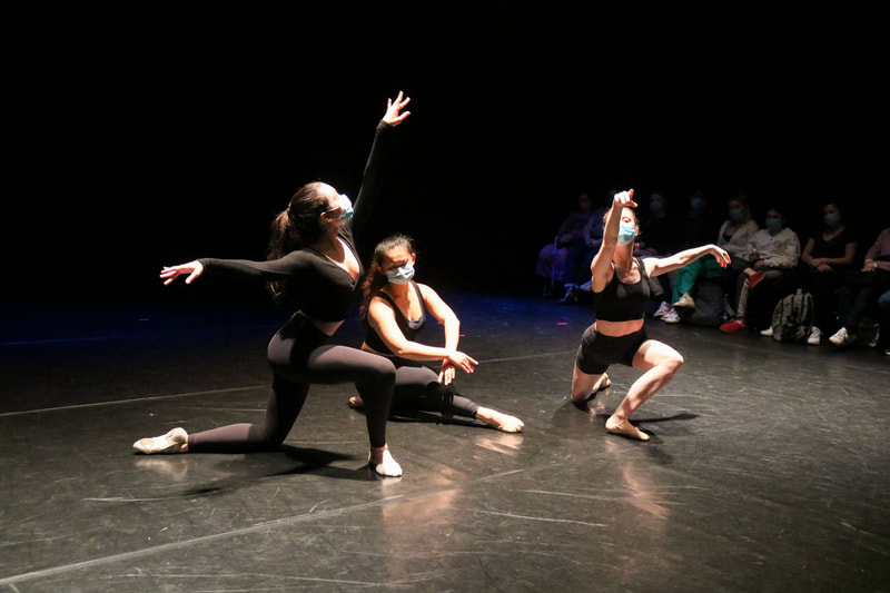 Three dancers in black outfits and blue masks. Center dancers is sitting with arms and legs crossed, two dancers on the sides are kneeling with arms in arabesque.